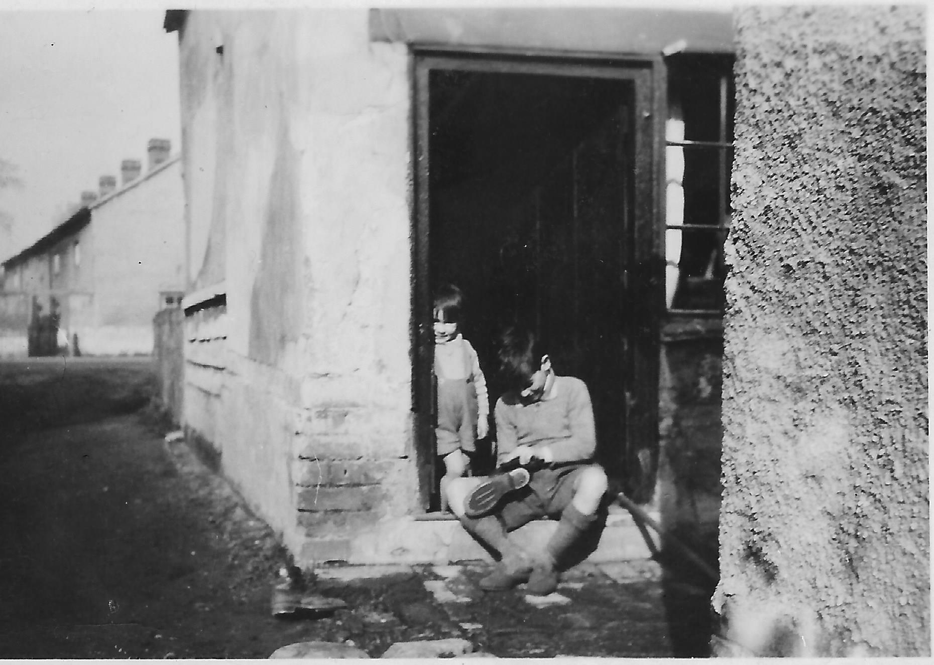 Brian Arbon at back door of terrace house with Robert behind